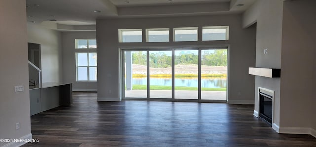 unfurnished living room with a towering ceiling, dark hardwood / wood-style floors, a tray ceiling, and a water view