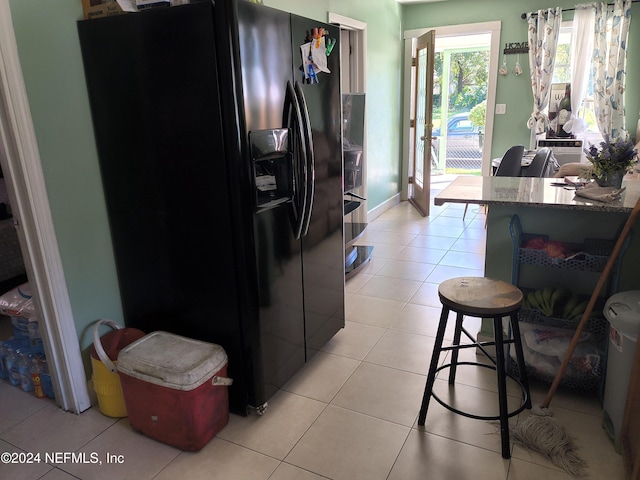 kitchen featuring light tile patterned flooring, stone counters, and black fridge with ice dispenser