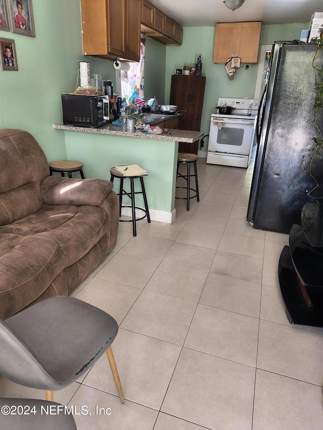 kitchen featuring light tile patterned flooring, a breakfast bar area, kitchen peninsula, and black appliances