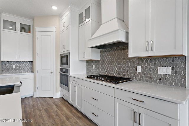 kitchen featuring appliances with stainless steel finishes, custom exhaust hood, white cabinetry, and decorative backsplash