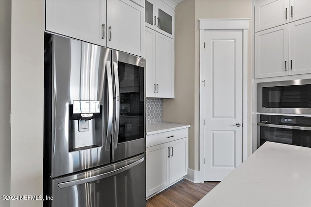 kitchen with appliances with stainless steel finishes, dark wood-type flooring, light stone counters, white cabinetry, and backsplash