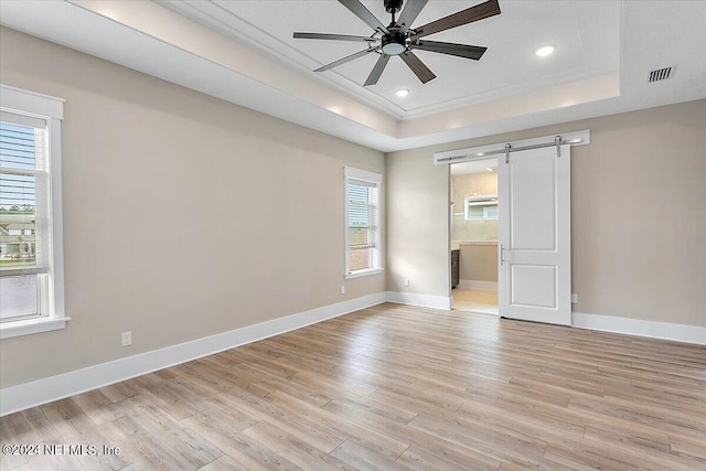 unfurnished bedroom with ensuite bathroom, multiple windows, a tray ceiling, a barn door, and ceiling fan