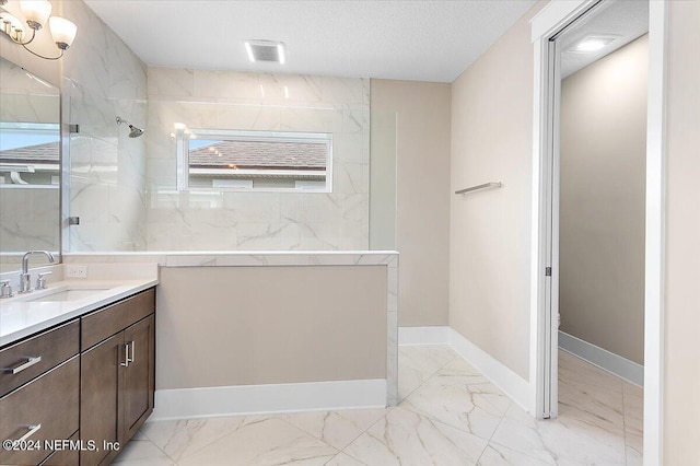 bathroom featuring a textured ceiling, a tile shower, and vanity