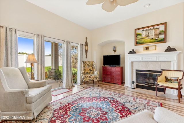 living room featuring hardwood / wood-style floors, a tile fireplace, and ceiling fan