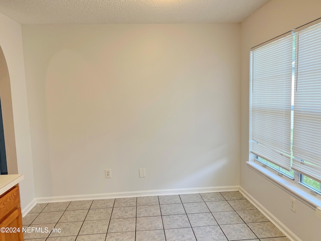 empty room with a textured ceiling and light tile patterned floors