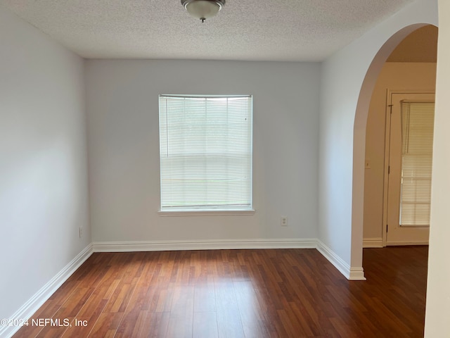 spare room with a textured ceiling, a healthy amount of sunlight, and dark hardwood / wood-style flooring