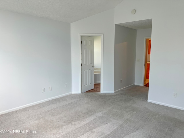 carpeted empty room featuring vaulted ceiling and a textured ceiling