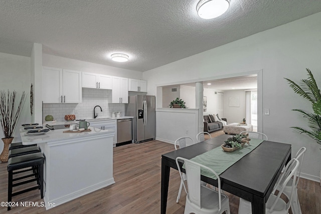 kitchen with a textured ceiling, appliances with stainless steel finishes, wood-type flooring, and white cabinets