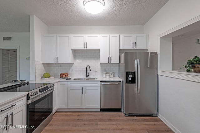 kitchen featuring sink, light wood-type flooring, stainless steel appliances, white cabinets, and decorative backsplash