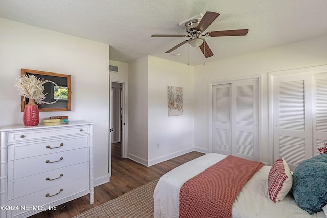 bedroom with multiple closets, a textured ceiling, dark hardwood / wood-style floors, and ceiling fan