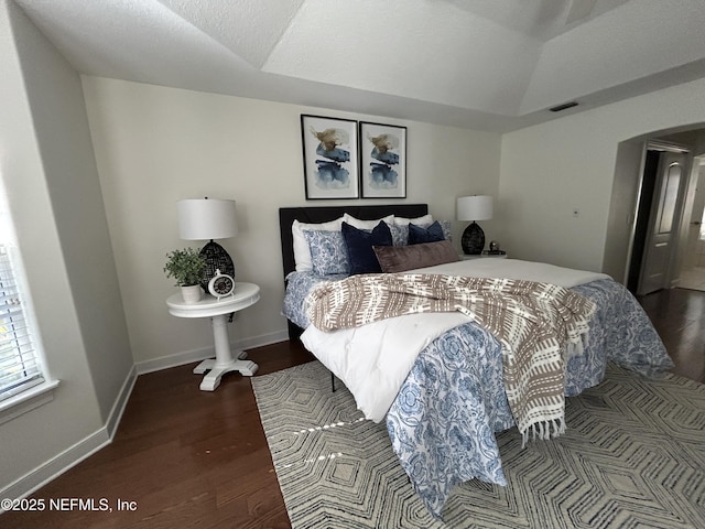 bedroom with arched walkways, visible vents, vaulted ceiling, wood finished floors, and baseboards