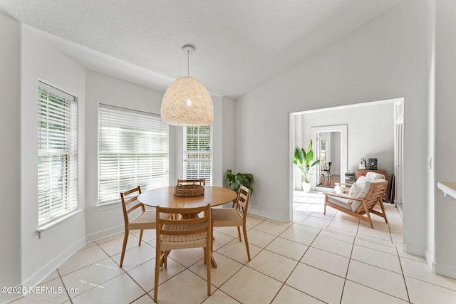 dining area with lofted ceiling, light tile patterned floors, baseboards, and a textured ceiling