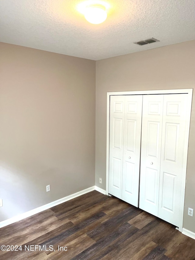 unfurnished bedroom featuring a textured ceiling, a closet, and dark hardwood / wood-style flooring