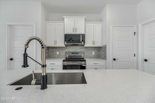 kitchen featuring sink, tasteful backsplash, light stone counters, white cabinets, and appliances with stainless steel finishes