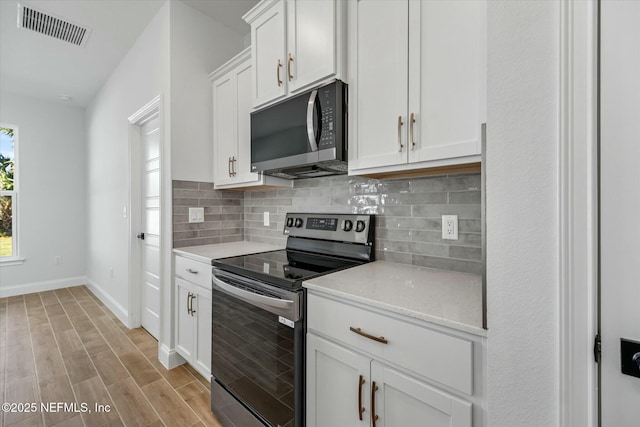 kitchen with white cabinets, appliances with stainless steel finishes, backsplash, and light hardwood / wood-style floors