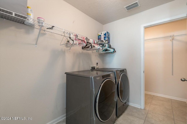 washroom with independent washer and dryer, light tile patterned floors, and a textured ceiling