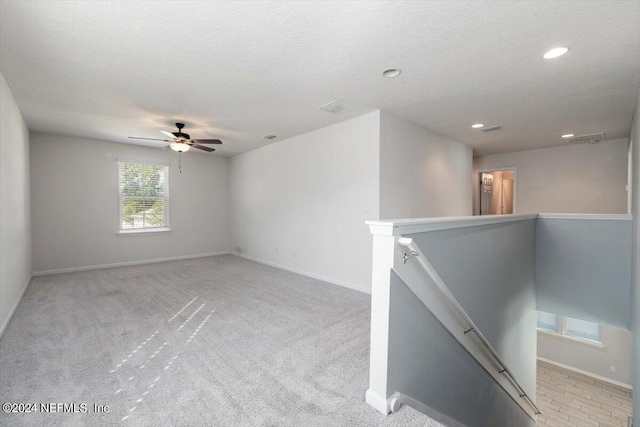 unfurnished room with a textured ceiling, ceiling fan, and light colored carpet