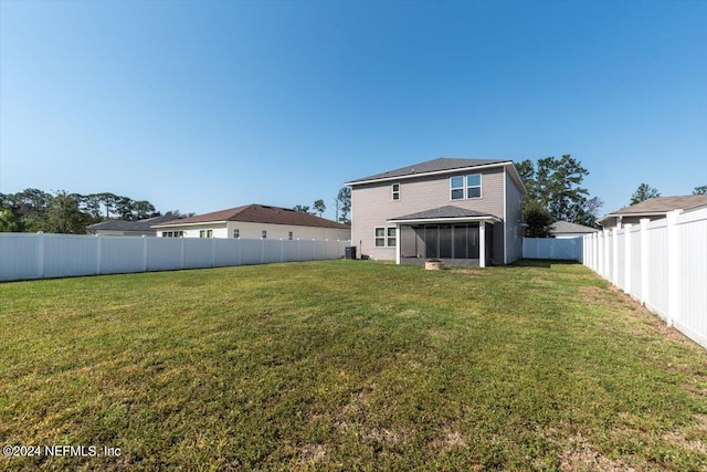 rear view of house featuring central AC, a sunroom, and a lawn