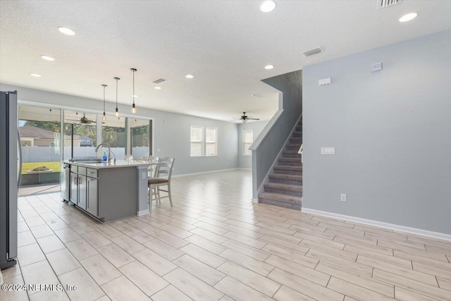 kitchen with ceiling fan, sink, a center island with sink, decorative light fixtures, and light wood-type flooring