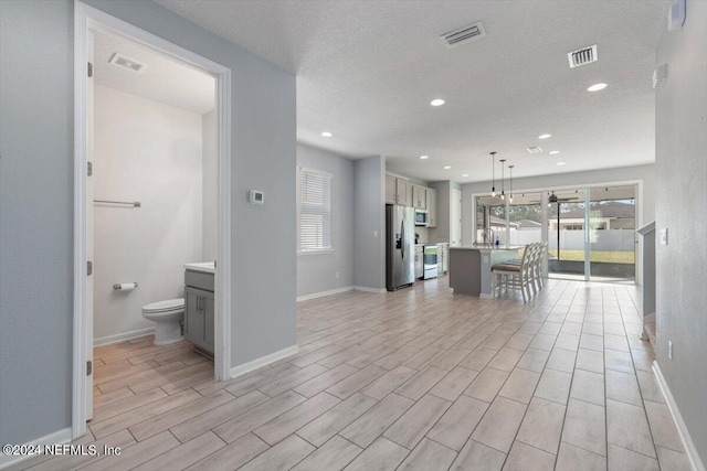 interior space featuring hanging light fixtures, a textured ceiling, a kitchen island with sink, light hardwood / wood-style flooring, and stainless steel appliances