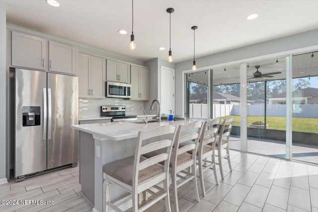 kitchen with gray cabinetry, pendant lighting, tasteful backsplash, a center island with sink, and appliances with stainless steel finishes