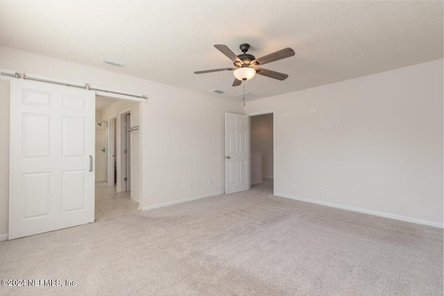 empty room with light carpet, a barn door, and ceiling fan