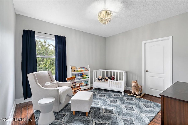 bedroom featuring a textured ceiling, a nursery area, and dark hardwood / wood-style floors