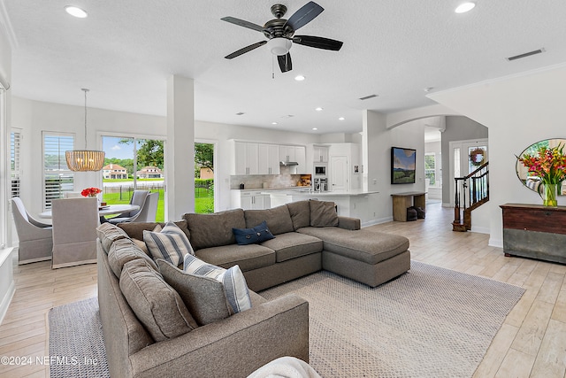 living room with a textured ceiling, light hardwood / wood-style flooring, a healthy amount of sunlight, and ceiling fan with notable chandelier