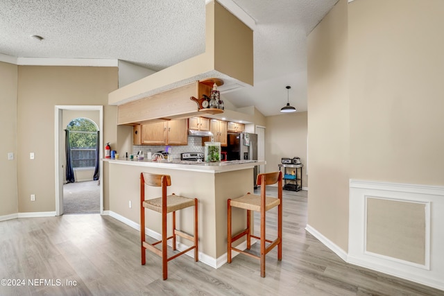 kitchen with lofted ceiling, a breakfast bar, kitchen peninsula, light hardwood / wood-style flooring, and backsplash