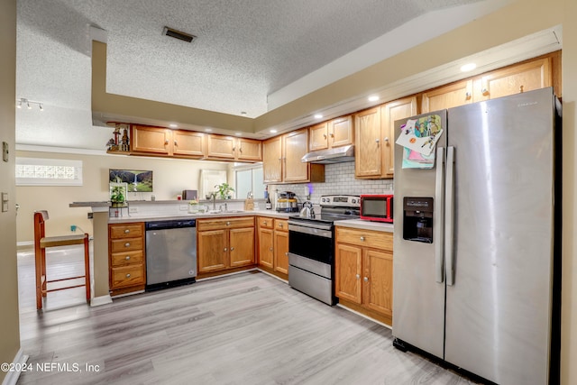 kitchen with kitchen peninsula, appliances with stainless steel finishes, light wood-type flooring, and a textured ceiling