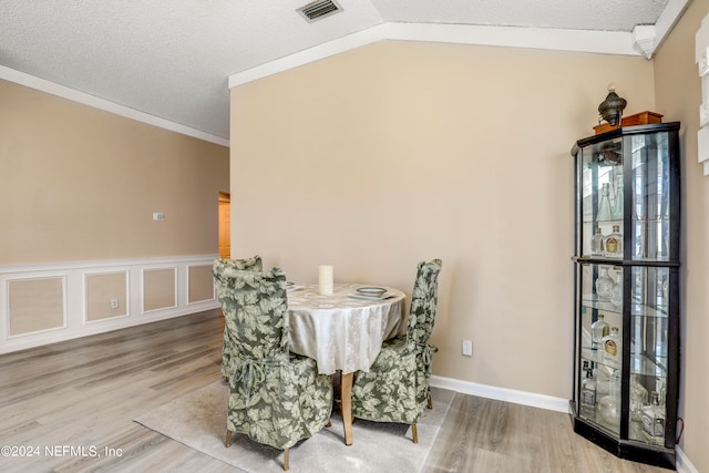 dining area featuring ornamental molding, lofted ceiling, wood-type flooring, and a textured ceiling