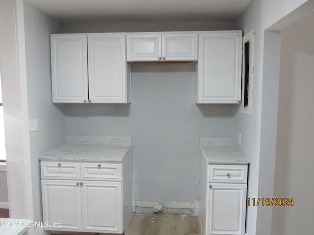 kitchen featuring white cabinets, light stone counters, and wood-type flooring