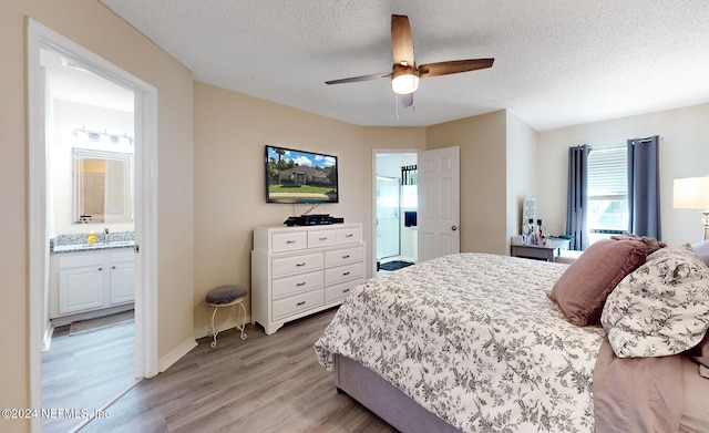 bedroom featuring ensuite bathroom, a textured ceiling, light hardwood / wood-style floors, and ceiling fan