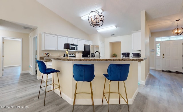 kitchen featuring pendant lighting, white cabinetry, a chandelier, appliances with stainless steel finishes, and light hardwood / wood-style floors