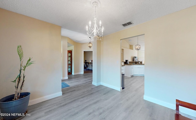 unfurnished dining area with a sink, a chandelier, light wood-style flooring, a textured ceiling, and baseboards