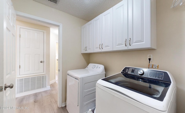 laundry room featuring washing machine and dryer, light wood-style flooring, cabinet space, a textured ceiling, and baseboards