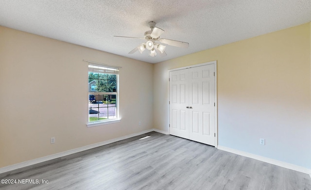 unfurnished bedroom with wood finished floors, a closet, a textured ceiling, baseboards, and ceiling fan