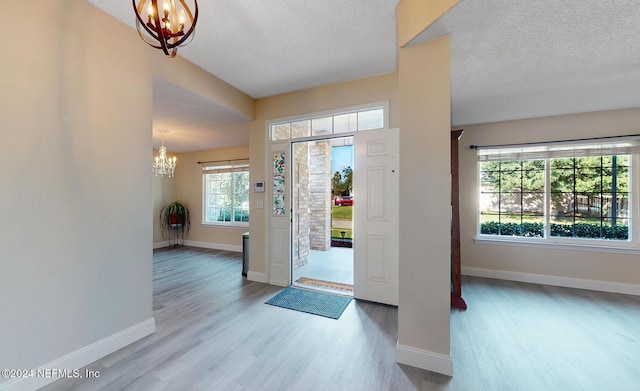 entryway with a chandelier, wood finished floors, baseboards, and a textured ceiling