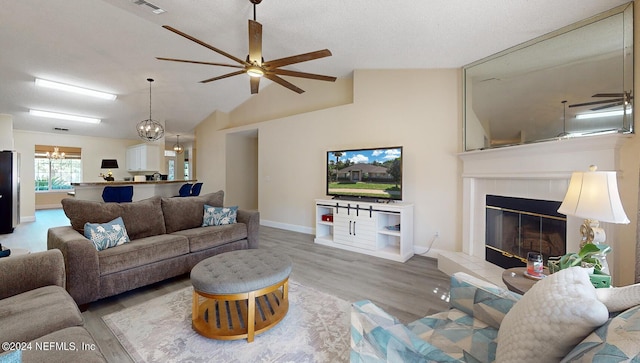 living room featuring a ceiling fan, wood finished floors, baseboards, a tiled fireplace, and a chandelier