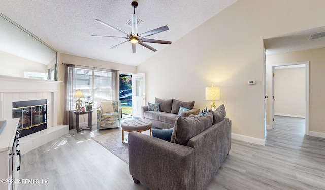 living room with ceiling fan, a textured ceiling, high vaulted ceiling, light hardwood / wood-style flooring, and a fireplace