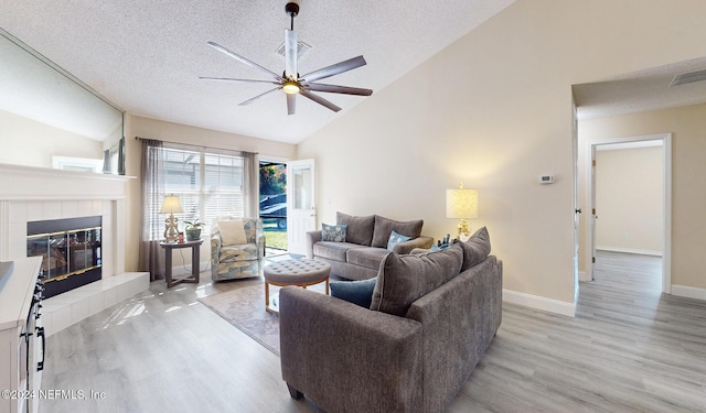 living room featuring vaulted ceiling, ceiling fan, wood finished floors, a textured ceiling, and a fireplace