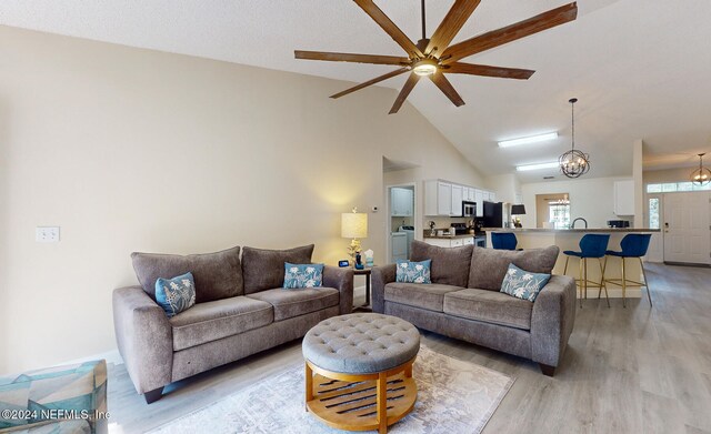 living room with washer / dryer, vaulted ceiling, light hardwood / wood-style flooring, and ceiling fan with notable chandelier