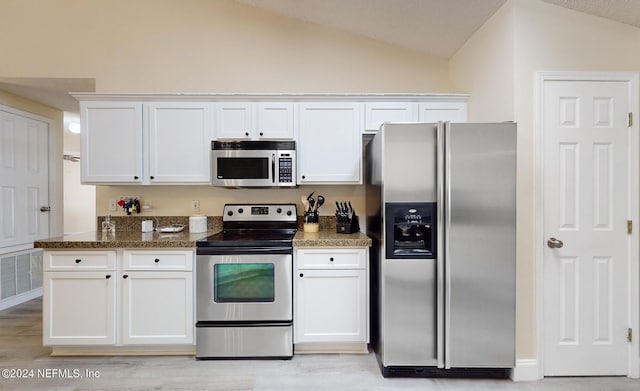 kitchen with appliances with stainless steel finishes, vaulted ceiling, white cabinetry, light wood-style flooring, and dark stone countertops