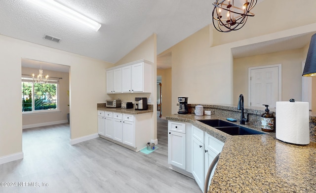 kitchen featuring sink, a textured ceiling, vaulted ceiling, white cabinets, and a chandelier