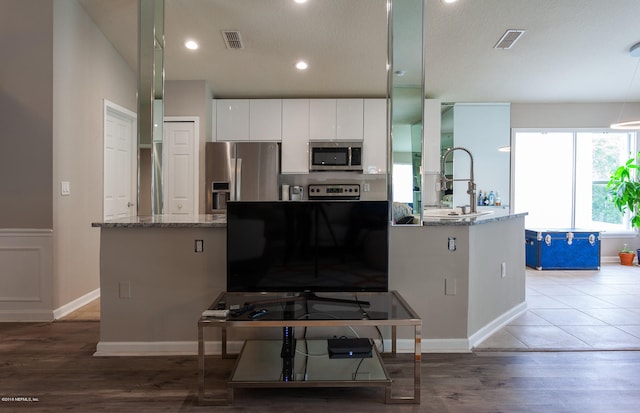 kitchen with white cabinets, hardwood / wood-style floors, a center island with sink, light stone countertops, and stainless steel appliances