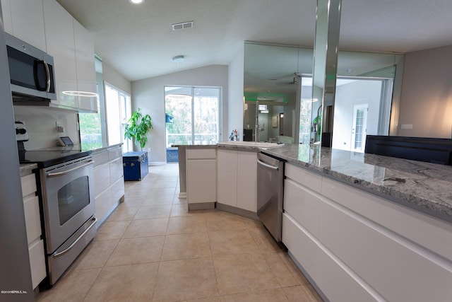 kitchen with white cabinets, light stone counters, vaulted ceiling, light tile patterned flooring, and stainless steel appliances