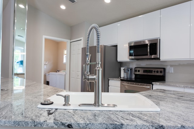 kitchen with appliances with stainless steel finishes, white cabinets, washer and dryer, and light stone countertops