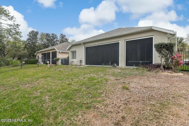rear view of house with stucco siding, a yard, and fence