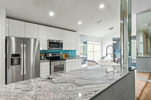 kitchen featuring decorative backsplash, white cabinets, stainless steel appliances, and a sink