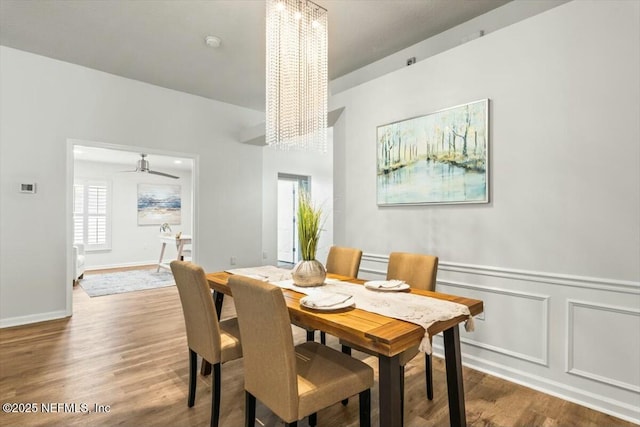 dining area with a decorative wall, wainscoting, an inviting chandelier, and wood finished floors